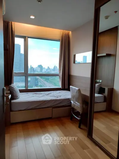 Cozy bedroom with city view, wooden flooring, and modern furnishings in a high-rise apartment.