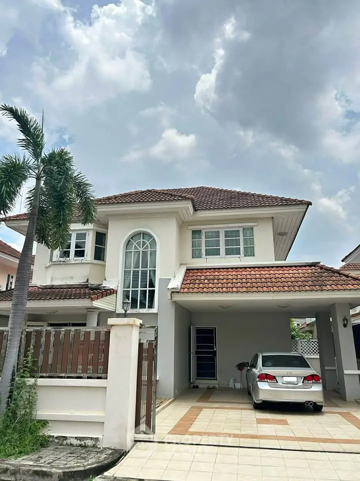 Charming two-story house with carport and palm tree in front yard under a cloudy sky.