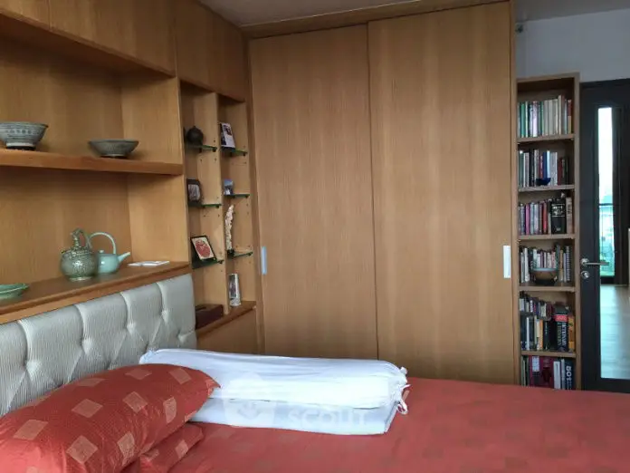 Cozy bedroom with built-in wooden shelves and wardrobe, featuring a comfortable bed and decorative items.