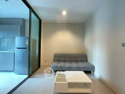 Modern living room with sleek sofa and glass partition leading to kitchen