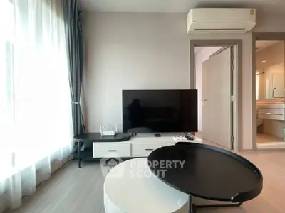 Modern living room with sleek furniture and large TV, featuring natural light from a window.