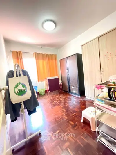 Spacious bedroom with wooden flooring and ample natural light, featuring a wardrobe and vibrant curtains.