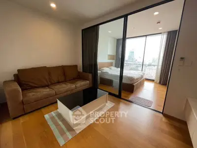Modern apartment with cozy living room and bedroom, featuring wooden flooring and large windows.