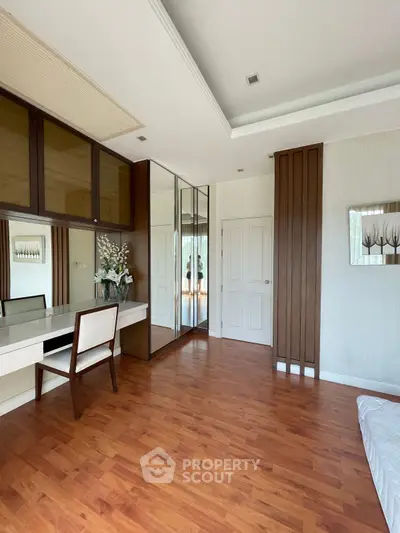 Spacious bedroom with wooden flooring and mirrored wardrobe, featuring elegant decor and ample natural light.