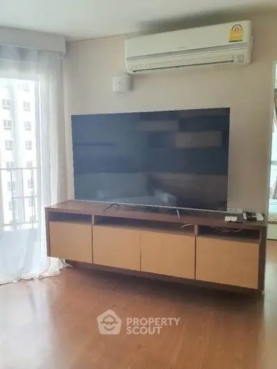 Modern living room with large TV and air conditioning, featuring natural light from balcony.