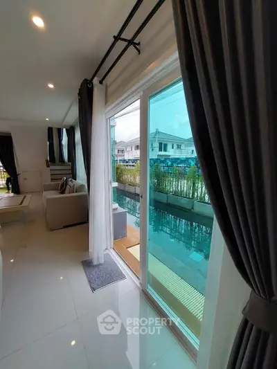 Modern living room with sliding glass doors leading to a poolside view, elegant curtains and sleek flooring.