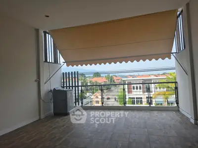 Spacious balcony with retractable awning and scenic neighborhood view.