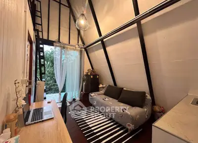 Charming A-frame living room with cozy sofa and workspace, featuring high ceilings and natural light.