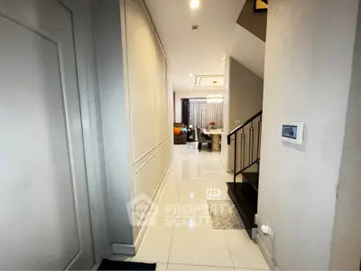 Modern hallway leading to a stylish living room with elegant decor and staircase.