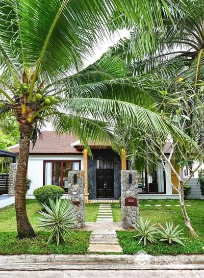 Charming tropical house with lush garden and palm trees, perfect for serene living.