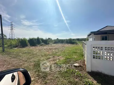 Spacious land plot with partial house view and clear blue sky, ideal for development.