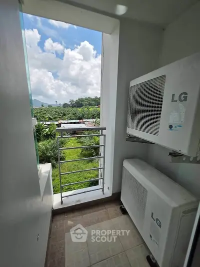 Compact balcony with air conditioning units and scenic view of lush greenery and blue sky.