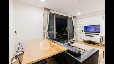 Spacious modern living room with large windows offering a night city view, complemented by sleek furniture and a cozy ambiance.