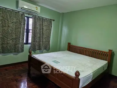 Spacious bedroom with wooden bed frame and green walls, featuring air conditioning and parquet flooring.