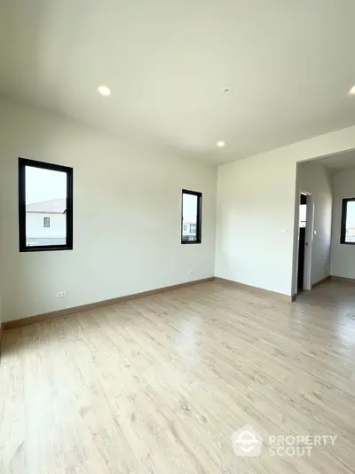 Spacious empty room with wooden flooring and natural light from windows