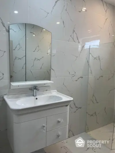 Modern bathroom with elegant marble tiles and sleek white vanity unit.