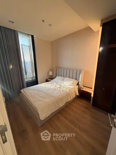 Cozy bedroom with modern design, featuring a plush bed and large window with city view.