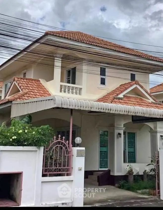 Charming two-story house with red-tiled roof and lush greenery in a serene neighborhood.