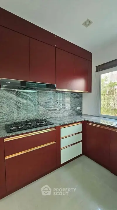 Modern kitchen with sleek cabinetry and gas stove, featuring elegant granite countertops and ample natural light.