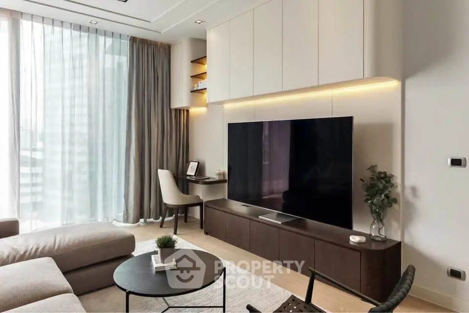 Modern living room with large TV, stylish furniture, and natural light from floor-to-ceiling windows.
