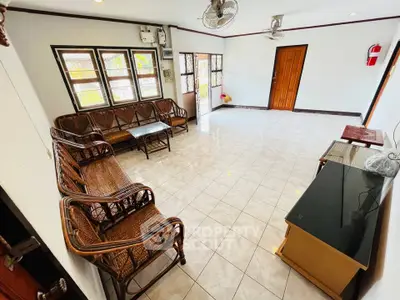 Spacious living room with tiled floor and wicker furniture, featuring large windows for natural light.