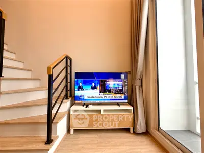 Modern living room with staircase and TV, featuring elegant decor and natural light.