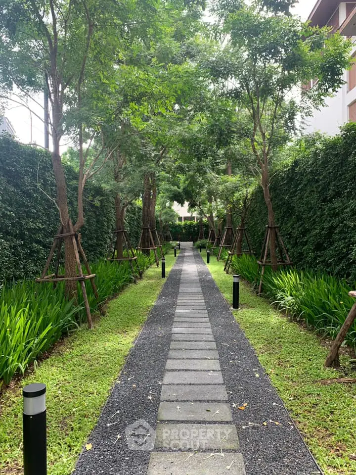 Serene garden pathway with lush greenery and modern lighting in a residential complex.