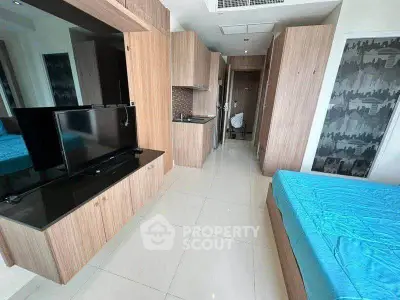 Modern studio apartment with sleek wooden cabinetry and vibrant blue bedding, featuring a compact kitchen area.