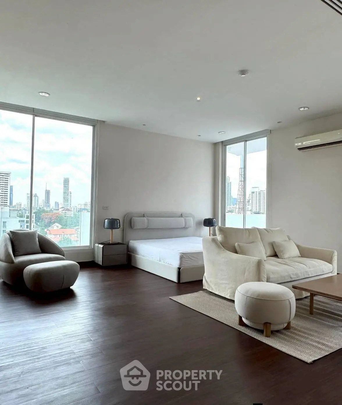 Spacious modern bedroom with city view, featuring elegant furniture and large windows.