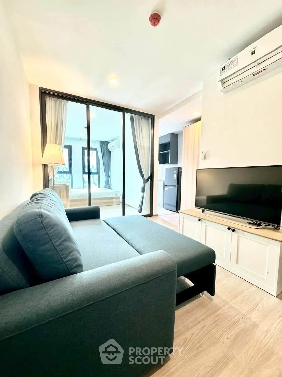 Modern living room with cozy sofa, TV, and open view to bedroom in stylish apartment.