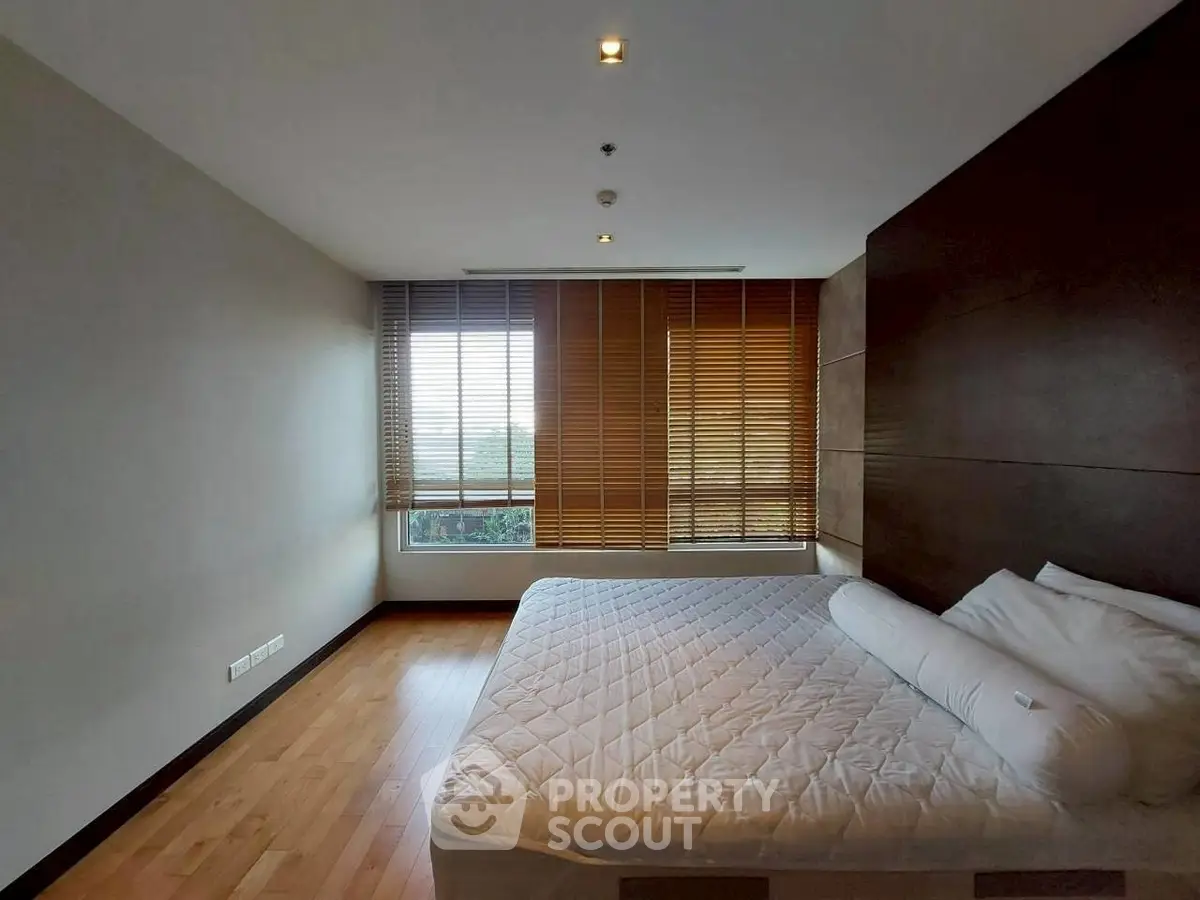 Spacious bedroom with wooden flooring and large window with blinds, offering a cozy and serene atmosphere.