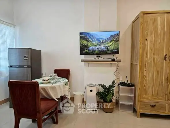 Cozy dining area with fridge, wooden wardrobe, and wall-mounted TV in a compact apartment.