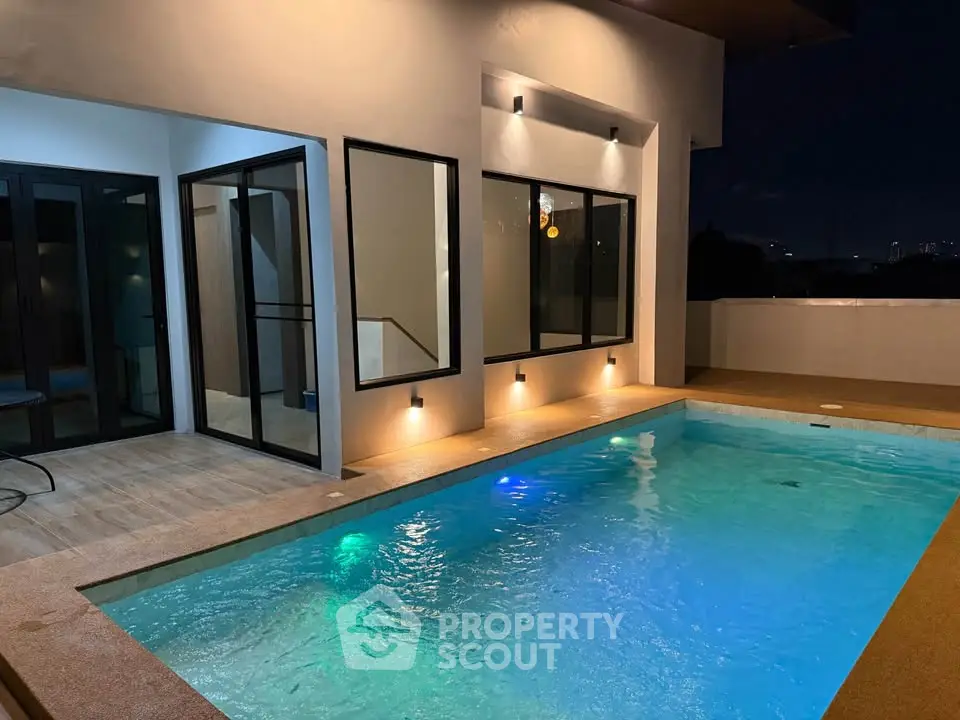 Luxurious modern home with illuminated private pool and stylish exterior lighting at night.