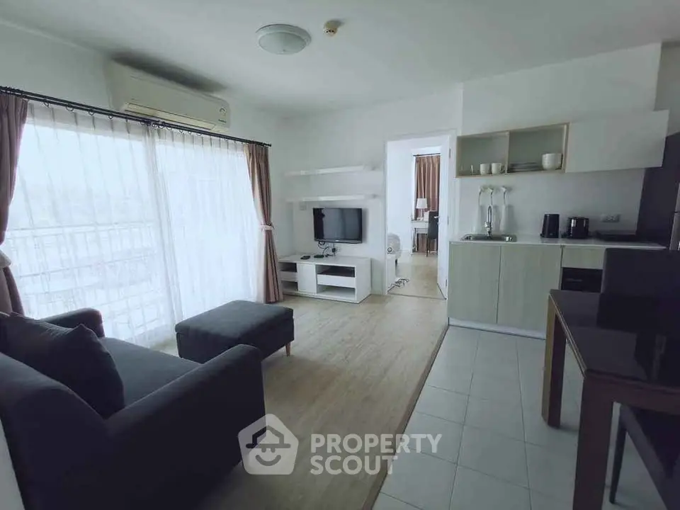 Modern living room with open kitchen and natural light, featuring stylish furniture and appliances.
