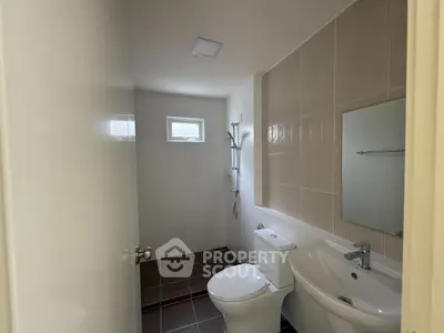 Modern bathroom with sleek fixtures and neutral tiles, featuring a shower and compact design.