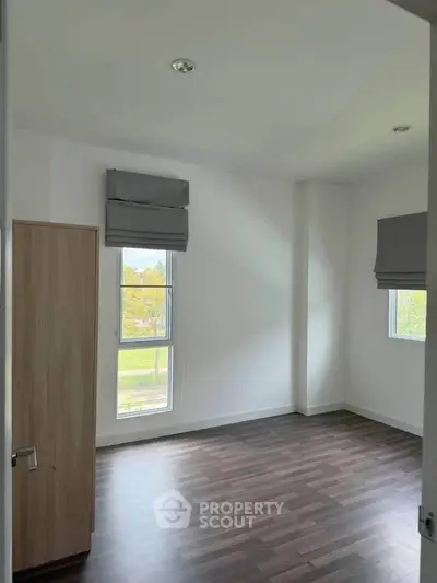 Spacious empty bedroom with large windows and wooden flooring, perfect for customization.