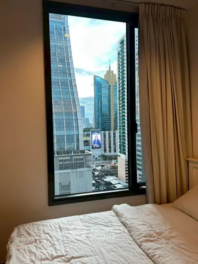 Modern bedroom with city view through large window in urban high-rise.