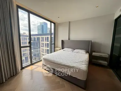 Modern bedroom with large windows offering a stunning city view, featuring a stylish bed and elegant flooring.