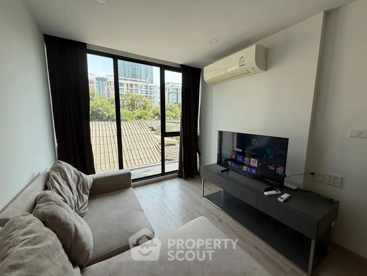 Modern living room with large window and city view, featuring cozy sofa and flat-screen TV.
