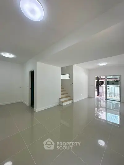 Spacious modern living room with glossy tiled floors and staircase, perfect for contemporary living.