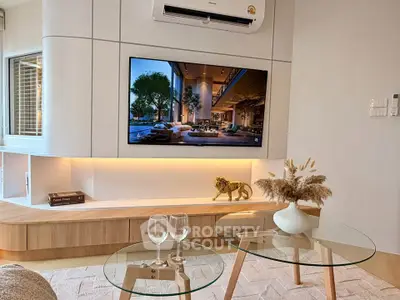Modern living room with stylish decor and mounted TV, featuring elegant glass tables and ambient lighting.