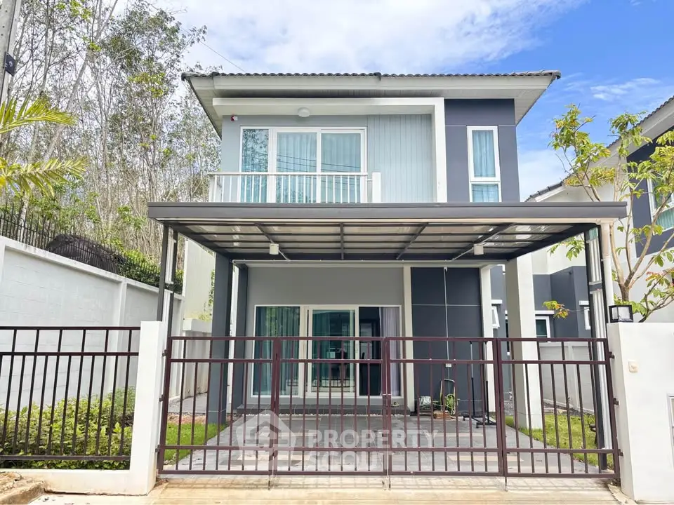 Modern two-story house with balcony and gated entrance, featuring sleek design and lush surroundings.