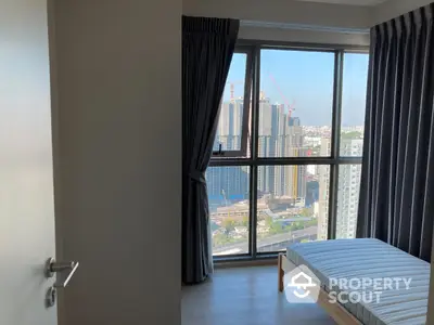 Bright and airy bedroom with large windows offering a stunning city view, complemented by a comfortable mattress and elegant curtains.