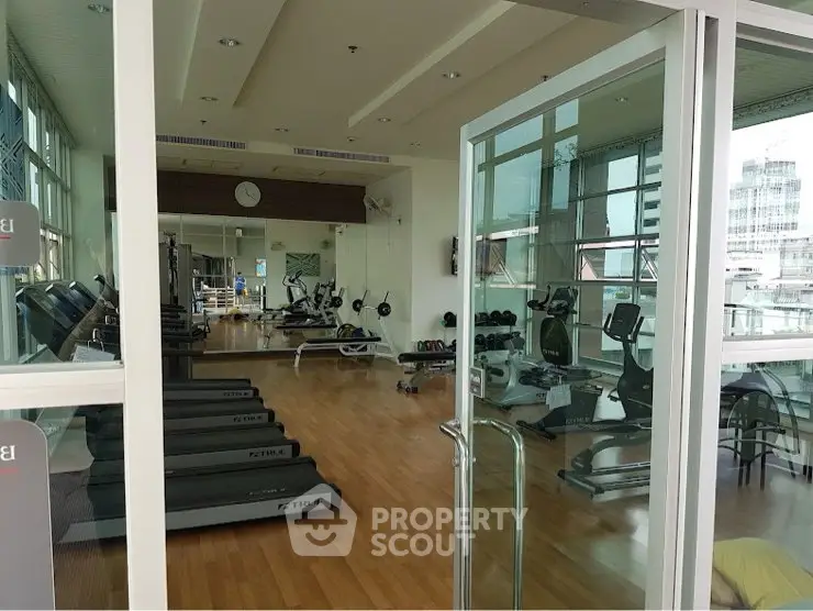 Spacious gym with modern equipment and large windows offering city views.