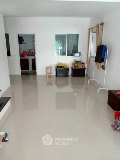 Spacious living area with glossy tiled flooring and minimal furnishings.