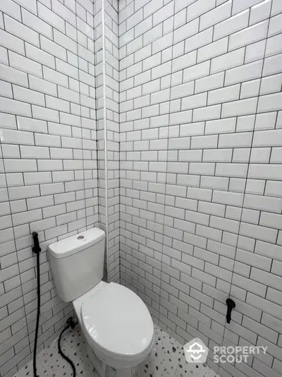 Pristine white-tiled bathroom corner featuring a modern toilet, showcasing a clean and minimalist design with speckled flooring.