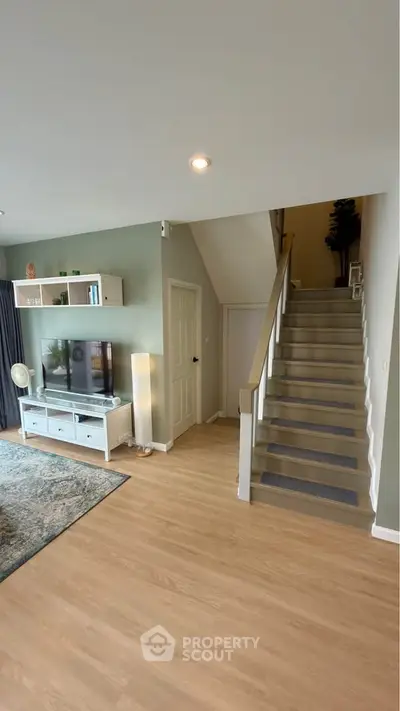 Modern living room with staircase and stylish decor, featuring a TV unit and wooden flooring.