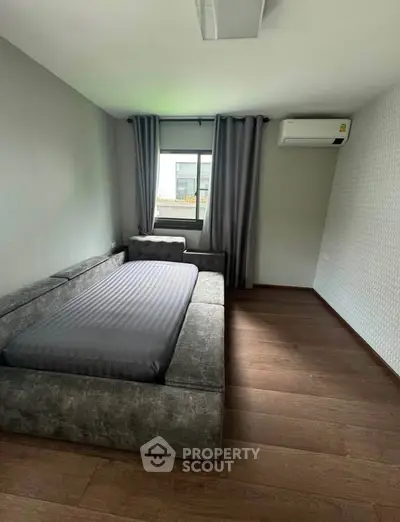 Modern bedroom with stylish gray sofa bed and air conditioning, featuring wooden flooring and natural light.