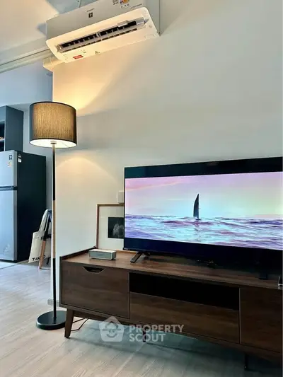 Modern living room with sleek TV setup and stylish floor lamp, featuring a minimalist design and air conditioning.