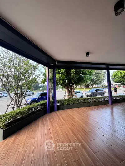 Spacious covered balcony with wooden flooring and street view, ideal for relaxation.